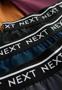 Quatre paires de shorts en noir, turquoise et bordeaux, dotés de ceintures élastiques avec le texte "NEXT" en blanc. Tissu en coton doux.