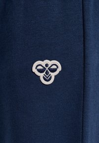 Mörkblått tyg med en texturerad yta, med en vit broderad bi-logotyp med mörkblå accenter placerad framträdande.