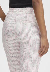 Pantalones de patrones multicolores con un diseño de rayas rosa y blanco, que cuentan con una cintura elástica y bolsillos traseros, confeccionados en una tela ligera.