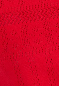 Rode gebreide stof met een gestructureerd patroon van kleine, open stipontwerpen en zigzaglijnen over het oppervlak.