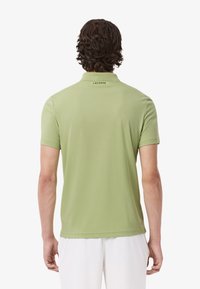 Camisa polo de tejido verde claro, de mangas cortas, con cuello acanalado y detalle del logo en la parte posterior. Textura suave con un corte clásico.