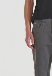 Jeans de mezclilla gris con un ligero estiramiento, que presentan un diseño clásico de cinco bolsillos, botones metálicos y costuras de contraste.