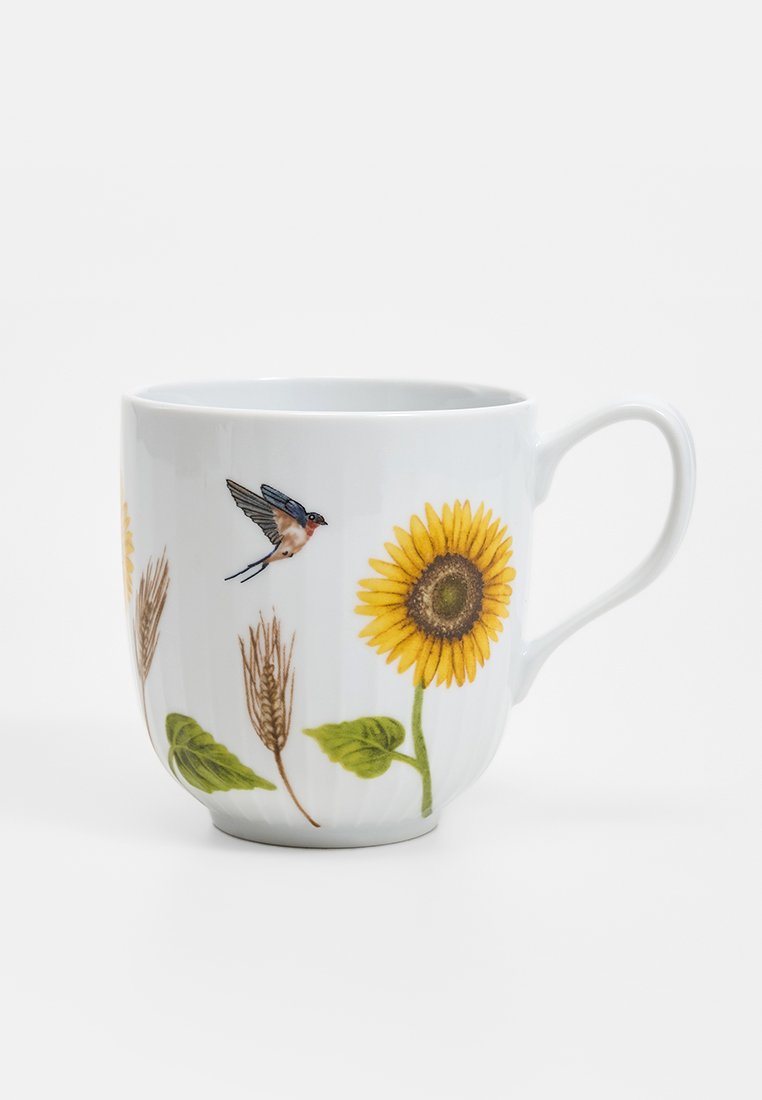Biały ceramiczny kubek z ilustracjami słonecznika, ptaka i pszenicy. Projekt zawiera żywe kolory i szczegółowe akcenty.