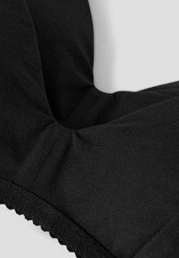 Black fabric garment with soft texture, featuring gathered design and scalloped edge detail. Smooth material enhances overall appearance.