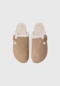 Tan suede clogs with a fluffy cream faux fur lining, backless design, and a side buckle detail. Smooth texture, rounded toe shape.