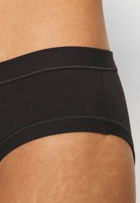Slip di cotone nero con una texture liscia, fascia in vita elastica e cuciture piatte, che enfatizzano un design minimale e una vestibilità focalizzata sul comfort.