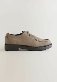 Pantof beige din suede cu vârf rotunjit, talpă din cauciuc negru contrastant și cusături decorative pe margini. Dispune de închidere cu șiret.