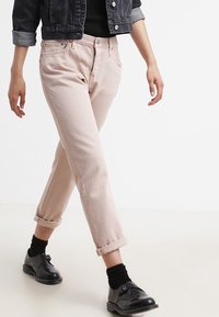 Vaqueros rosa claro de corte relajado, con puños enrollados y diseño de cinco bolsillos, combinados con un cárdigan negro y zapatos negros.