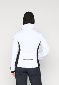 Λευκό μπουφάν με μόνωση και ψηλό γιακά, με μαύρες πλευρικές πινακίδες και λεπτομέρεια λογότυπου στο πίσω μέρος. Λείος υφάσματος και προσαρμοσμένη εφαρμογή.