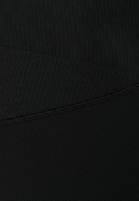 Crni materijal za aktivnu odjeću s rebrastom teksturom, koji sadrži horizontalnu šavnu detalj. Čini se da je materijal rastezljiv i prilagođen tijelu.