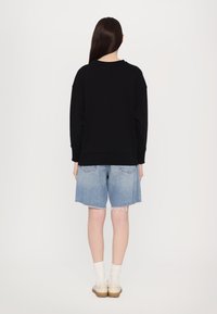 Čierna oversized mikina s dlhými rukávmi, skombinovaná so svetlomodrými denimovými šortkami s rozstrapkanými okrajmi a dvoma zadnými vreckami.