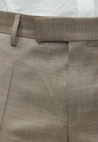 Pantaloni beige su misura con una texture liscia, presentano una parte anteriore piatta, tasche laterali e una cintura classica.