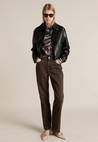 Black leather cropped jacket, animal print top, brown high-waisted trousers, and beige pointed flats. Black sunglasses complete the look.