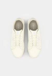 Baskets en cuir blanc avec des bouts ronds, des lacets plats et une doublure intérieure texturée. Présente un petit logo sur le côté et au talon.