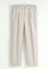 Pantalons beiges avec taille élastique, bouton proéminent, poches latérales et design droit suspendus sur un fond blanc.