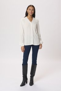 White long-sleeve blouse with lace trim and button closure, paired with navy skinny jeans and knee-high black leather boots.