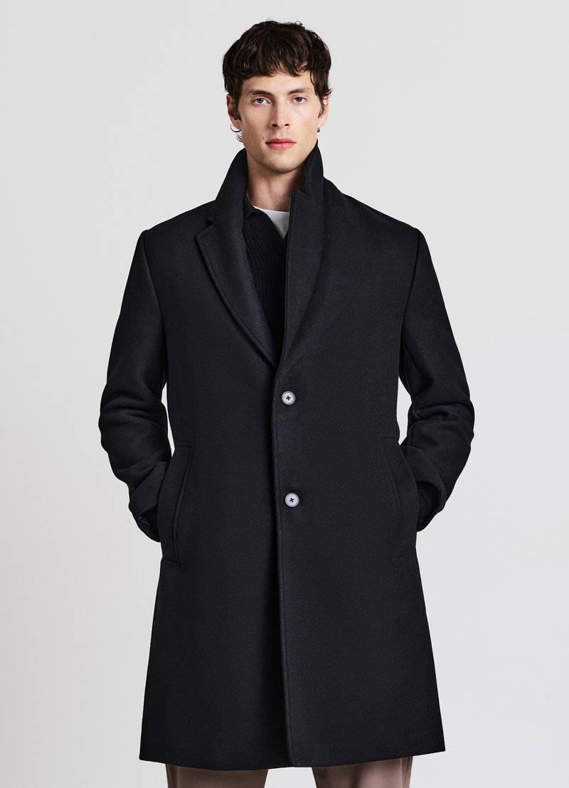 Cappotto in lana nera con colletto con risvolto, due bottoni e tasche laterali. Presenta un design pulito e una texture liscia, adatto a vari tipi di abbigliamento.