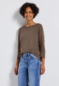 Braunes Langarmoberteil mit Rundhalsausschnitt, kombiniert mit hellblauen weiten Jeans. Glatte Textur und lässige Passform.