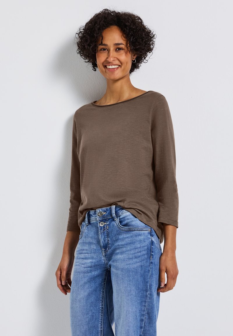Braunes Langarmoberteil mit Rundhalsausschnitt, kombiniert mit hellblauen weiten Jeans. Glatte Textur und lässige Passform.