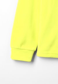 Manga de sudadera de forro polar amarillo fluorescente con puño de canalé; la textura suave y la superficie lisa contrastan con el color vibrante.