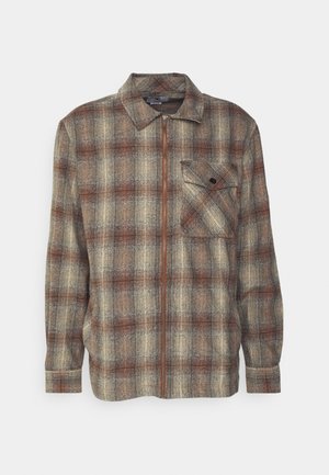 Camicia con zip a quadri nei colori beige, marrone e ruggine. Presenta un colletto, maniche lunghe e una tasca sul petto con bottone. Tessuto testurizzato.