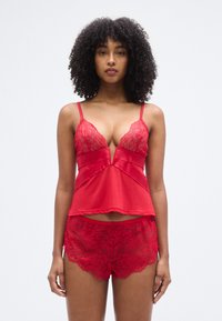 Ensemble de lingerie rouge comprenant un caraco en satin avec des accents en dentelle et un décolleté en V profond, accompagné de shorts assortis bordés de dentelle. Texture lisse.