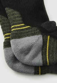 Calcetines negros y verde oscuro con secciones de punta y talón grises. Presentan rayas amarillas y una textura acanalada para mayor agarre y comodidad.