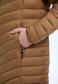 Bruine pufferjas met een doorstikt ontwerp en horizontale stiksels. Zijzak met ritsdetail. Gladde, glanzende stoftextuur.