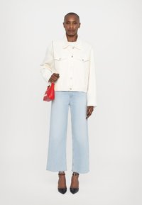 White denim jacket with front pockets, paired with light blue wide-leg jeans and black pointed-toe heels. Red handbag with gold chain strap.