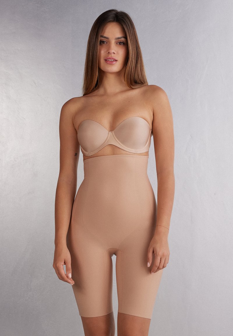 Nude naadloze vormgevende body met een strapless ontwerp, lengte tot halverwege de bovenbenen en glad, rekbaar materiaal voor het accentueren van de contouren.