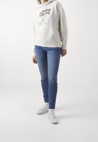 Krémová mikina s designem leopardího vzoru, přední kapsa; světle modré skinny džíny; bílé tenisky s detaily krajky.