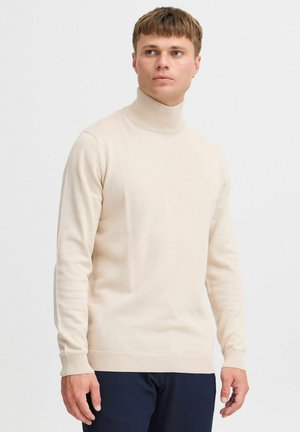 Suéter de cuello alto beige en suave tejido de punto, diseño ajustado, puños y dobladillo acanalados, con una textura suave y apariencia minimalista.