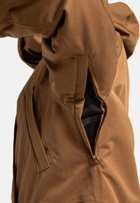 Braune Jacke mit teilweise geöffnetem Unterarm-Belüftungsreißverschluss, der einen schwarzen Netzstoff als Futter darunter zeigt.