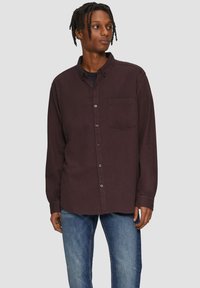 Chemise boutonnée pour homme de couleur violet foncé avec une poche poitrine, à manches longues et coupe décontractée, associée à un jean bleu. Texture de tissu lisse.