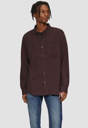 Donkere paarse button-up shirt voor heren met een borstzak, lange mouwen en een relaxte pasvorm, gecombineerd met blauwe jeans. Soepele textuur van de stof.