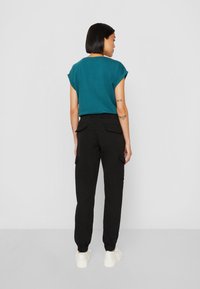 Teal kortärmad topp som är kombinerad med högmidjade svarta cargobyxor med sidfickor och elastiska muddarna. Modellen bär vita sneakers.