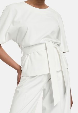 Blouse blanche à coupe décontractée, manches courtes, encolure ronde, et ceinture nouée mettant en valeur la taille. Confectionnée dans un tissu lisse et léger.