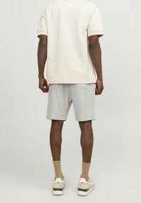 Camiseta de manga corta beige, pantalones cortos grises con un bolsillo, zapatillas color crema con acentos, calcetines hasta el tobillo, vista desde la parte posterior.