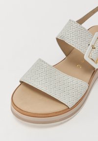 White woven strap sandals with two wide, flat bands. Features a chunky sole with a light brown base and a rectangular buckle accent.