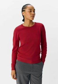 Pull à col rond rouge en tissu doux, doté de longues manches et d'un ourlet côtelé ; assorti à un pantalon gris cintré. Texture lisse.