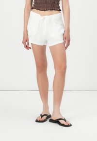 Hvite linshorts med snor i livet, med to frontlommer og en avslappet passform, sammen med svarte flip-flops.