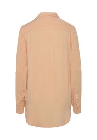 Long-sleeve, peach-colored shirt made of soft fabric. Features a back yoke, buttoned cuffs, and a curved hemline.