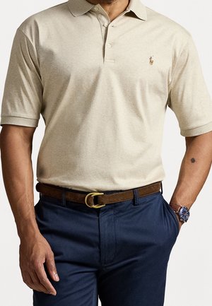 Mand iført beige kortærmet polo, brun bælte, marineblå bukser og et armbåndsur med en brun rem og blå urskive.