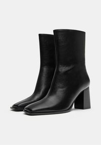 Crne kožne čizme do gležnja s kvadratnim vrhom, visokim blok ravnim potpeticama, glatkom teksturom i vertikalnim šavom duž bokova.