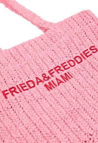 Różowa torba tote z plecionego materiału, z wytłoczonym czerwoną czcionką napisem "FRIEDA & FREDDIES MIAMI" z przodu.