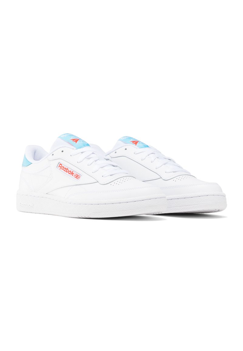 Sneakers atletici bianchi con dettagli blu e logo rosso, dotati di una tomaia in pelle liscia, punta perforata e suola in gomma testurizzata.
