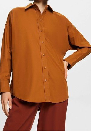 Camisa de botón de manga larga marrón, hecha de una tela suave con cuello puntiagudo y un corte relajado, con un dobladillo curvado y botones visibles.