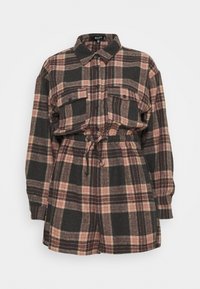 Plaid shirt dress in black, pink, and beige with a collar, two chest pockets, and an adjustable drawstring waist. Soft, textured fabric.