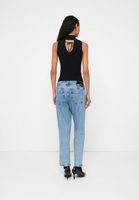 Top preto sem mangas com detalhe de laço nas costas, combinado com jeans azul claro de cintura alta, com corte relaxado e texturas subtis.