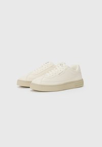 Beige canvas sneakers met een gladde textuur, ronde neus en rubberen zool. Heeft bijpassende veters en logo-detail op de tong.